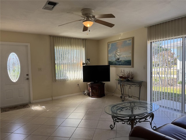 tiled living room featuring baseboards, ceiling fan, visible vents, and a healthy amount of sunlight