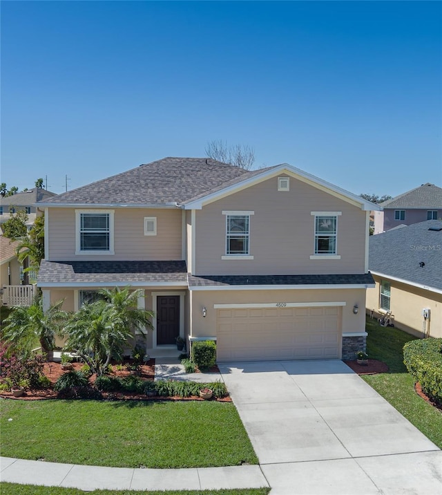 traditional-style home featuring an attached garage, concrete driveway, a front lawn, and a shingled roof