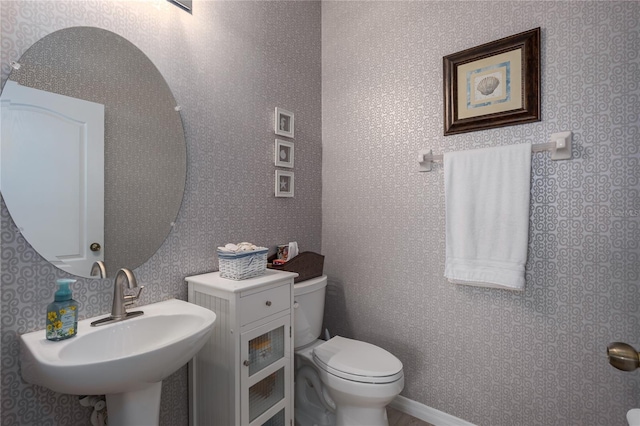 half bathroom featuring wallpapered walls, toilet, and a sink