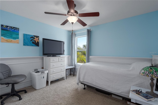 carpeted bedroom featuring wainscoting and ceiling fan