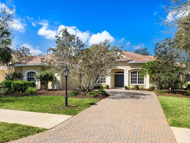 view of front of home featuring a front yard, a tiled roof, decorative driveway, and stucco siding