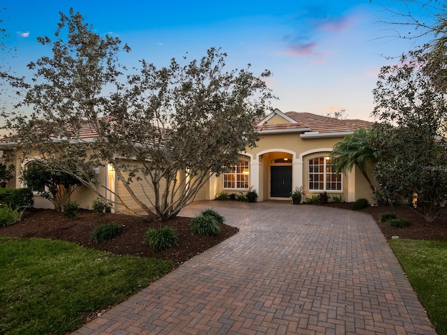 view of front of property with stucco siding, a tiled roof, an attached garage, and decorative driveway