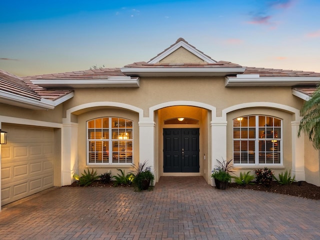 entrance to property with stucco siding, decorative driveway, an attached garage, and a tiled roof