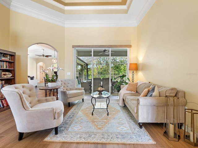 living room with crown molding, ceiling fan, wood finished floors, a sunroom, and arched walkways