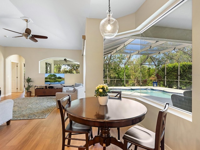 dining area featuring arched walkways, wood finished floors, a ceiling fan, and a sunroom