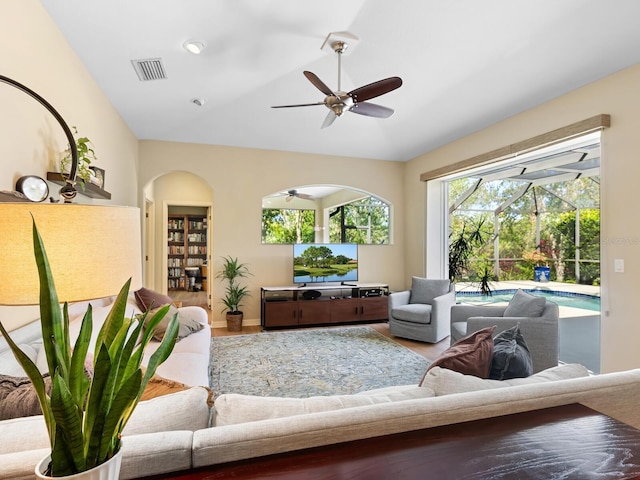 living area featuring visible vents, a ceiling fan, arched walkways, a sunroom, and vaulted ceiling