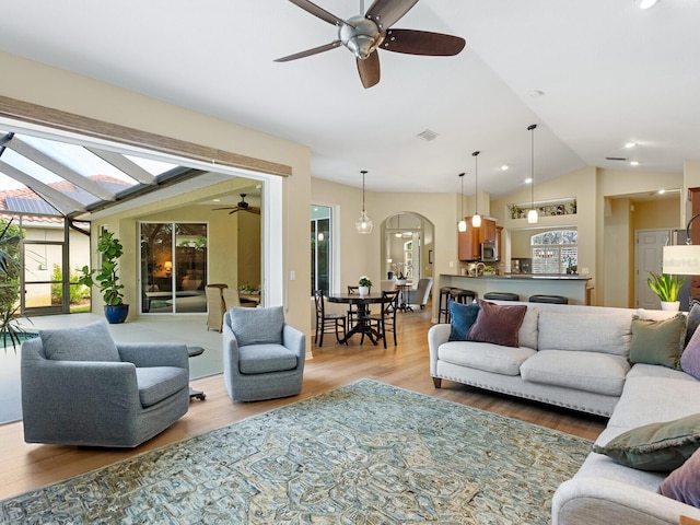 living room featuring visible vents, ceiling fan, vaulted ceiling, light wood-style floors, and arched walkways