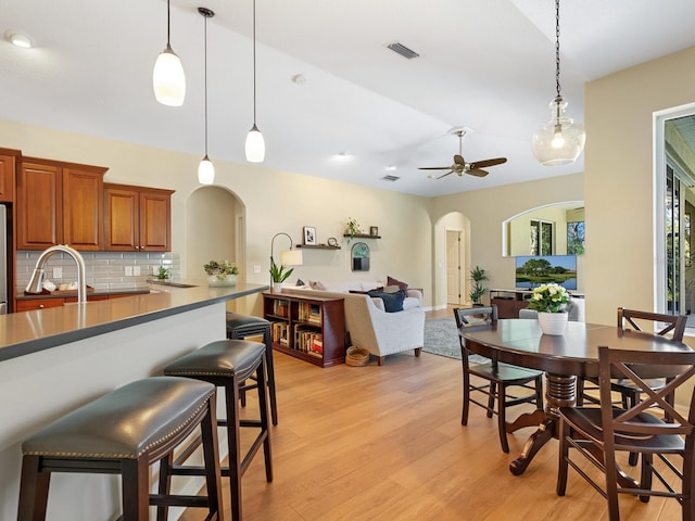 dining space with light wood-type flooring, arched walkways, visible vents, and a ceiling fan