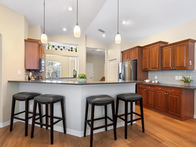 kitchen with dark countertops, a breakfast bar area, light wood-style floors, and stainless steel fridge with ice dispenser