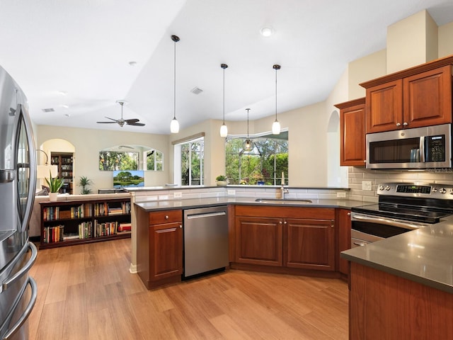 kitchen featuring light wood finished floors, appliances with stainless steel finishes, a peninsula, and a sink