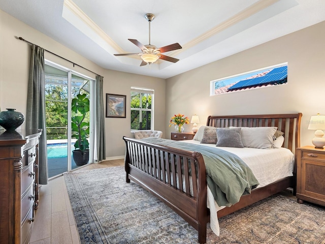 bedroom with access to exterior, ceiling fan, a tray ceiling, and wood finished floors