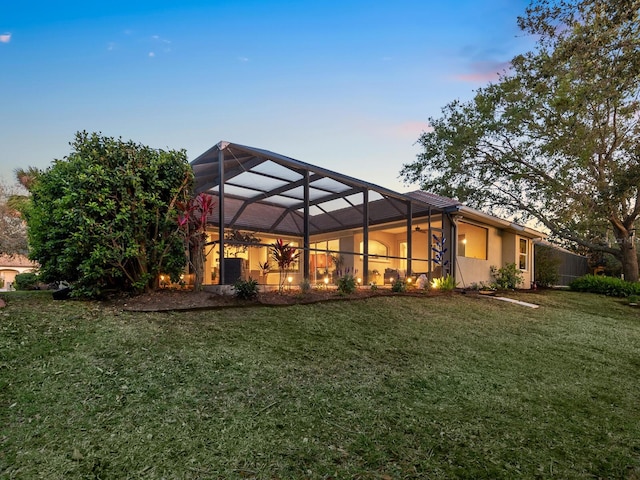 back of house at dusk featuring a lanai and a lawn