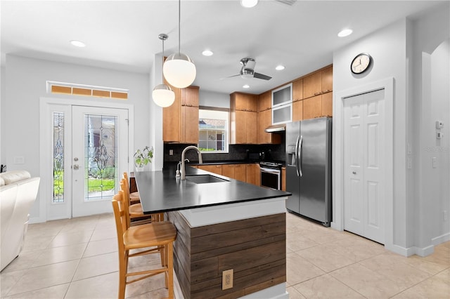 kitchen featuring dark countertops, appliances with stainless steel finishes, brown cabinets, a peninsula, and a sink