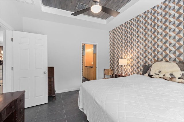 bedroom with a tray ceiling, an accent wall, ceiling fan, dark tile patterned flooring, and baseboards