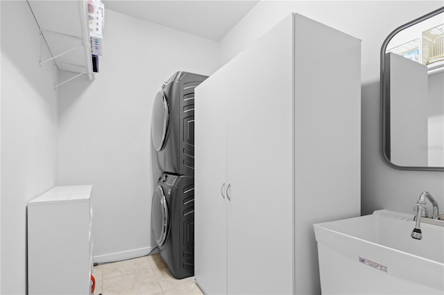 laundry area with light tile patterned floors, stacked washer and dryer, a sink, laundry area, and baseboards