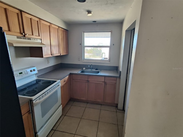 kitchen featuring white range with electric stovetop, freestanding refrigerator, under cabinet range hood, a sink, and light tile patterned flooring