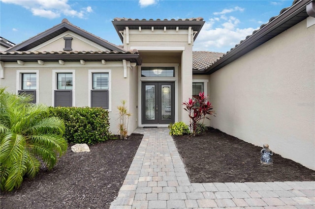 entrance to property with french doors, a tile roof, and stucco siding