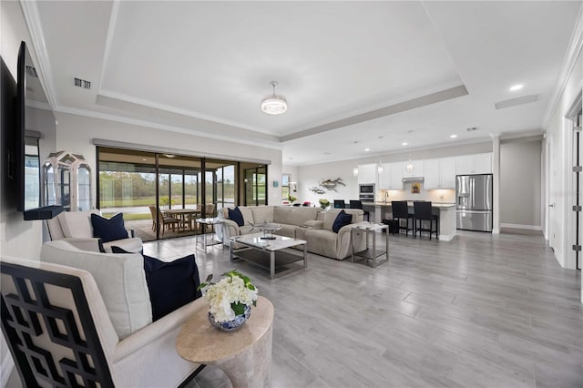 living area with visible vents, a tray ceiling, baseboards, and ornamental molding