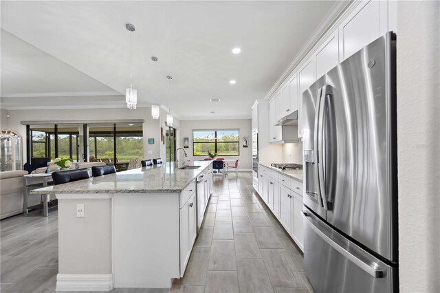 kitchen with under cabinet range hood, a sink, white cabinetry, appliances with stainless steel finishes, and a center island with sink