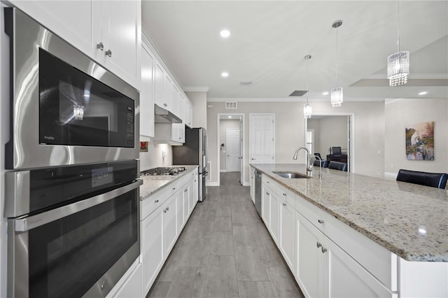 kitchen with appliances with stainless steel finishes, ornamental molding, white cabinets, a sink, and under cabinet range hood