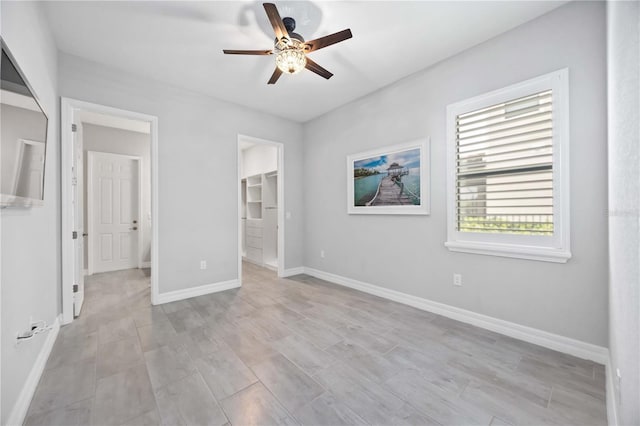 unfurnished bedroom with a spacious closet, a ceiling fan, and baseboards