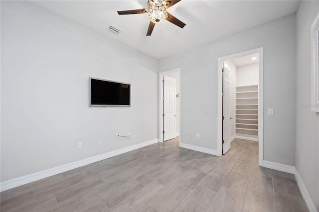 unfurnished bedroom with a walk in closet, a closet, visible vents, a ceiling fan, and baseboards