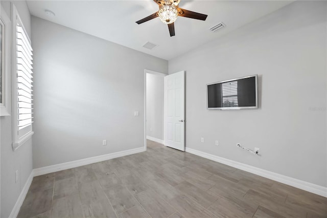 empty room featuring ceiling fan, a wealth of natural light, visible vents, and baseboards