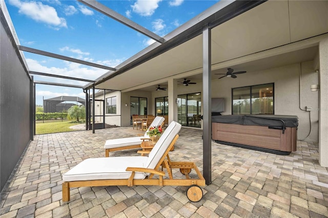 view of patio / terrace featuring a ceiling fan, outdoor dining space, glass enclosure, and a hot tub