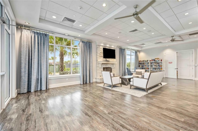 living room with a stone fireplace, wood finished floors, visible vents, baseboards, and a ceiling fan