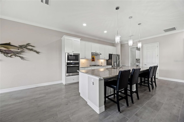 kitchen with appliances with stainless steel finishes, a large island with sink, ornamental molding, baseboards, and white cabinetry