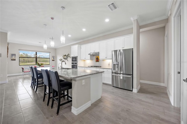 kitchen with appliances with stainless steel finishes, a center island with sink, ornamental molding, baseboards, and white cabinetry