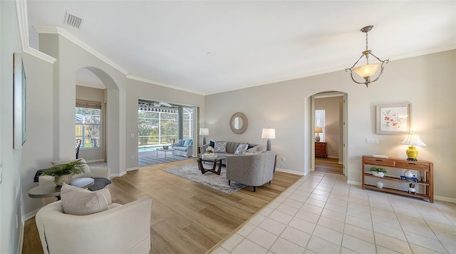 living area with ornamental molding, arched walkways, visible vents, and baseboards