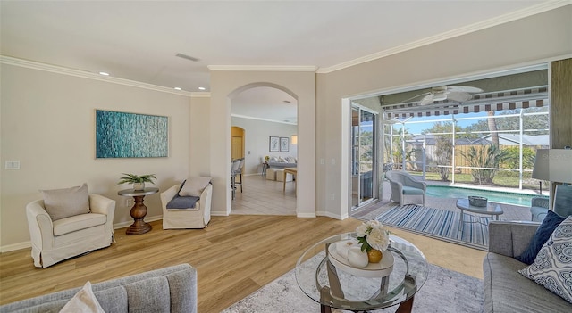 living area with arched walkways, ornamental molding, a ceiling fan, wood finished floors, and baseboards