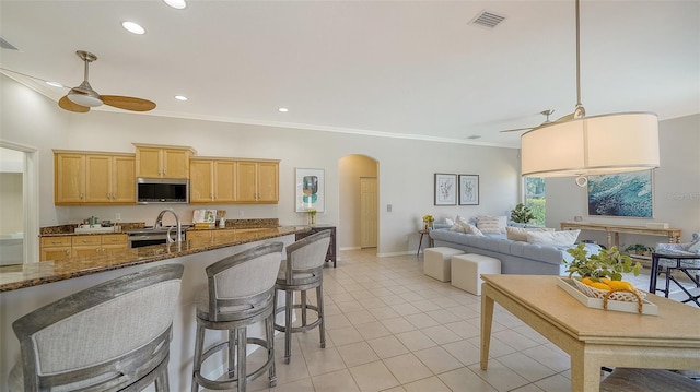 kitchen featuring arched walkways, crown molding, stainless steel appliances, light brown cabinets, and ceiling fan