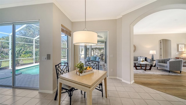 dining space featuring arched walkways, light tile patterned flooring, a sunroom, baseboards, and crown molding