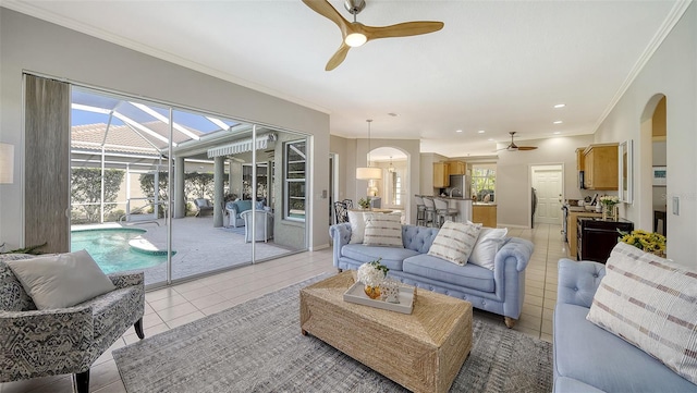 living room featuring arched walkways, ceiling fan, light tile patterned floors, a sunroom, and crown molding