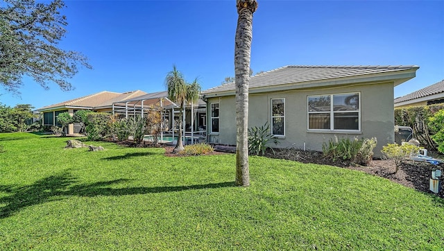 rear view of property with a yard, a lanai, and stucco siding