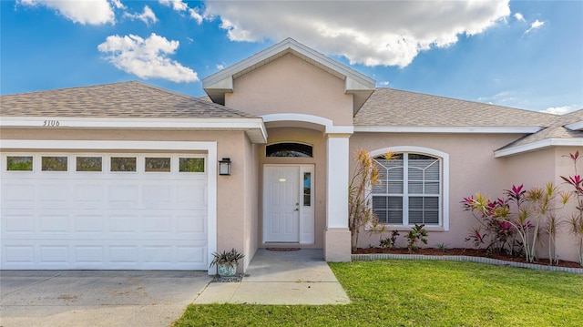 doorway to property featuring a garage, driveway, roof with shingles, a yard, and stucco siding