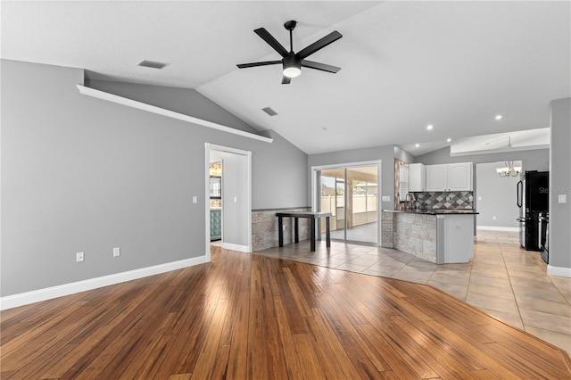 unfurnished living room with visible vents, vaulted ceiling, light wood-type flooring, baseboards, and ceiling fan with notable chandelier