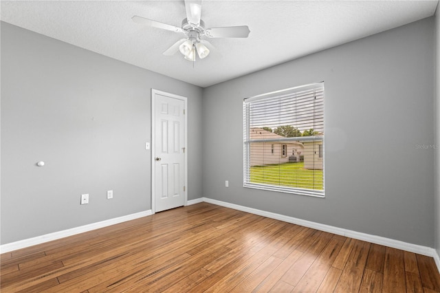 spare room with a textured ceiling, hardwood / wood-style floors, a ceiling fan, and baseboards