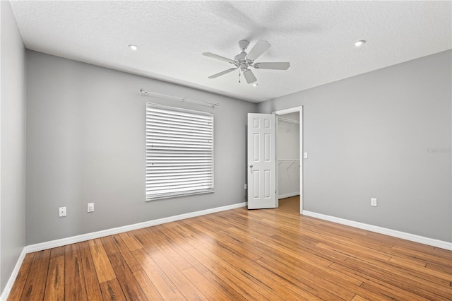 unfurnished bedroom featuring a textured ceiling, a ceiling fan, baseboards, light wood-style floors, and a spacious closet