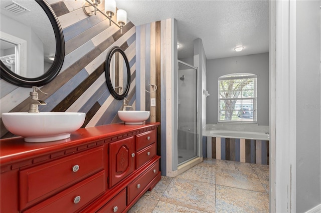 bathroom with stone tile flooring, a sink, a textured ceiling, and a shower stall