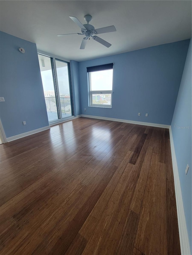 spare room with expansive windows, dark wood finished floors, a ceiling fan, and baseboards