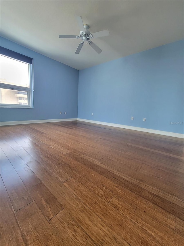 empty room featuring ceiling fan, baseboards, and dark wood finished floors