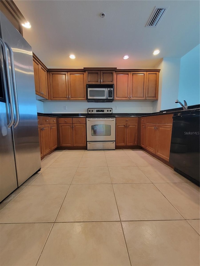 kitchen featuring light tile patterned floors, stainless steel appliances, dark countertops, visible vents, and brown cabinetry