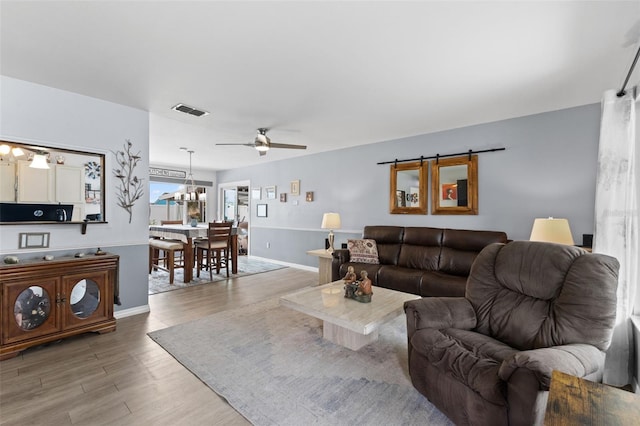 living area with visible vents, light wood-style flooring, ceiling fan with notable chandelier, and baseboards