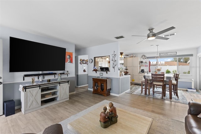 living area with light wood-type flooring, visible vents, and ceiling fan with notable chandelier