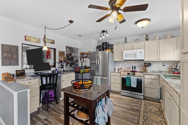 kitchen with decorative backsplash, hanging light fixtures, wood finished floors, and appliances with stainless steel finishes