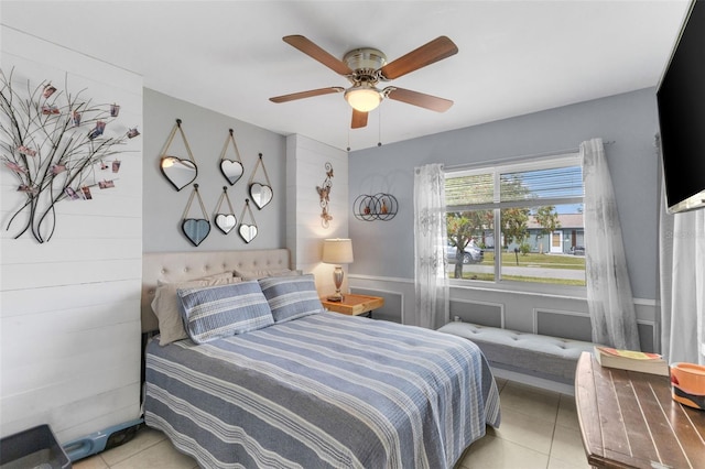 tiled bedroom with ceiling fan and wainscoting