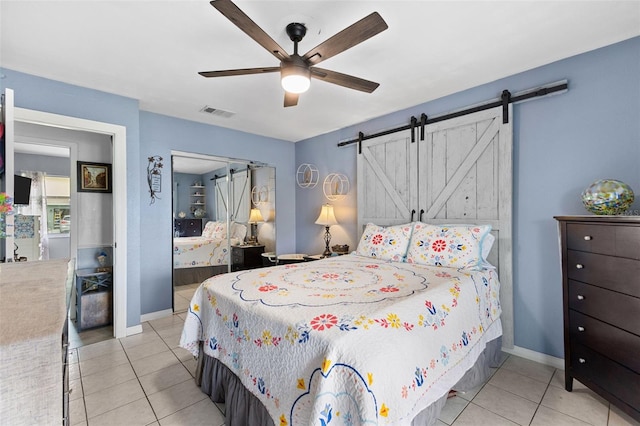 bedroom with a barn door, light tile patterned flooring, a ceiling fan, and baseboards